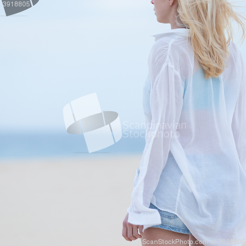 Image of Woman on sandy beach in white shirt at dusk. 