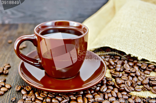 Image of Coffee in brown cup with grains and bag on board