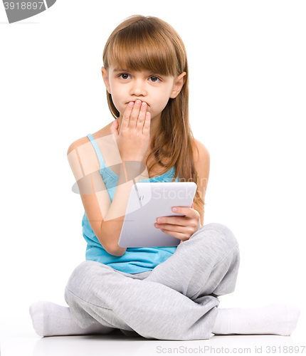Image of Young girl is using tablet while sitting on floor