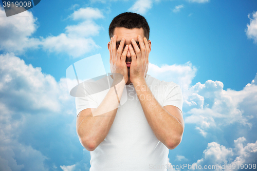 Image of man in white t-shirt covering his face with hands