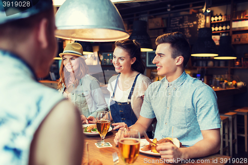 Image of happy friends eating and drinking at bar or pub