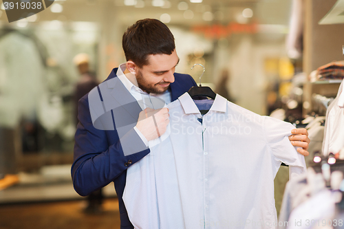 Image of happy young man choosing clothes in clothing store