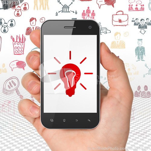 Image of Business concept: Hand Holding Smartphone with Light Bulb on display