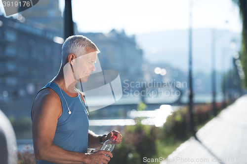 Image of senior jogging man drinking fresh water from bottle