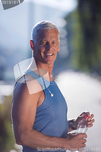 Image of senior jogging man drinking fresh water from bottle