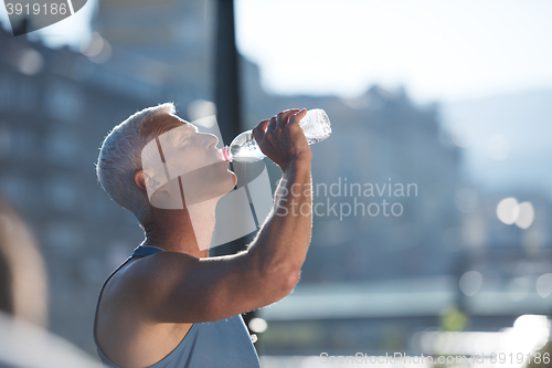 Image of senior jogging man drinking fresh water from bottle