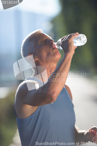 Image of senior jogging man drinking fresh water from bottle