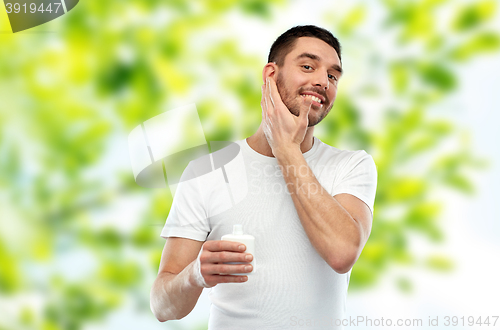 Image of happy young man applying cream or lotion to face