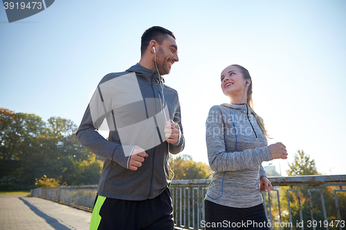 Image of happy couple with earphones running outdoors