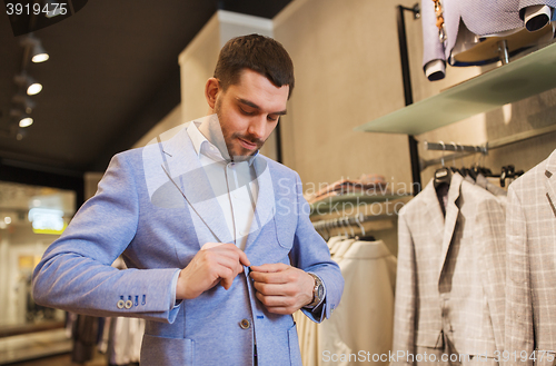 Image of happy young man trying jacket on in clothing store