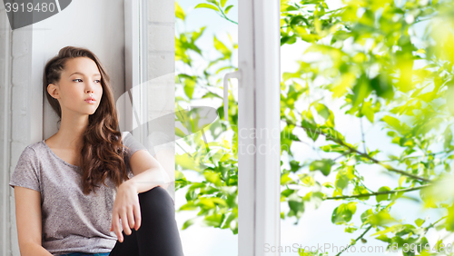 Image of sad pretty teenage girl sitting on windowsill