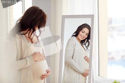 Image of happy pregnant woman looking to mirror at home