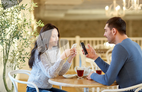 Image of happy couple with smartphones drinking tea at cafe