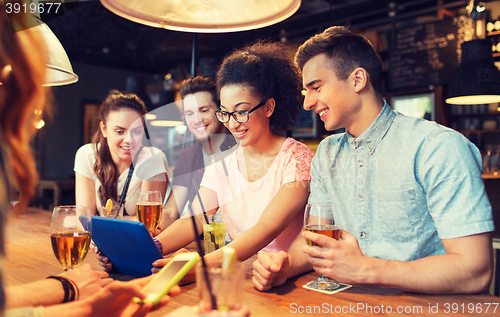 Image of happy friends with tablet pc and drinks at bar