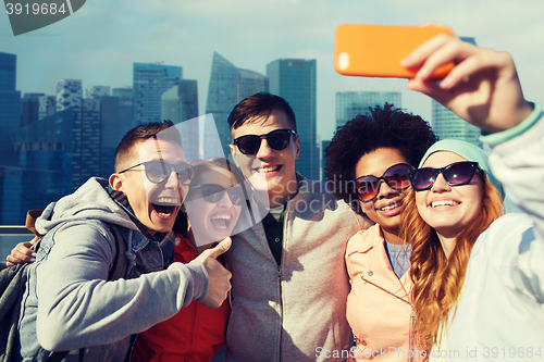 Image of smiling friends taking selfie with smartphone