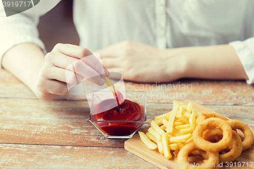 Image of close up of hand dipping french fries into ketchup