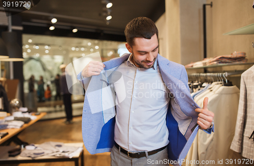 Image of happy young man trying jacket on in clothing store