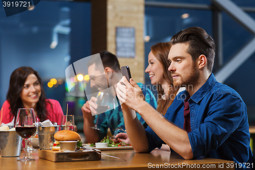 Image of man with smartphone and friends at restaurant
