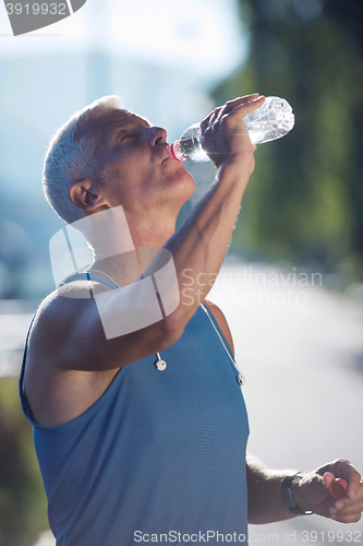 Image of senior jogging man drinking fresh water from bottle