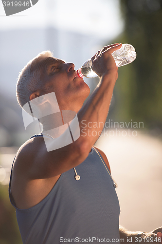 Image of senior jogging man drinking fresh water from bottle