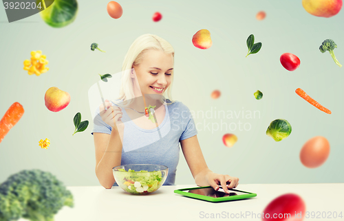 Image of smiling woman eating salad with tablet pc