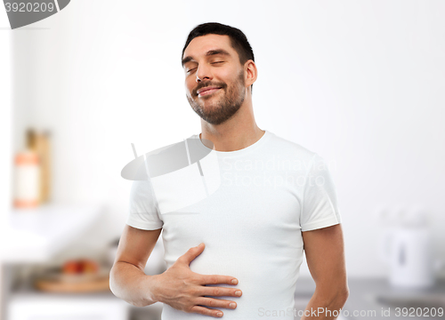 Image of happy full man touching tummy over kitchen