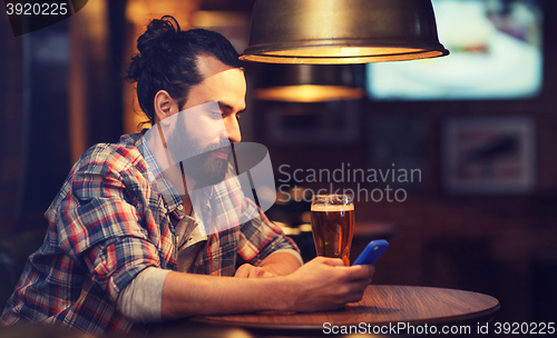 Image of man with smartphone and beer texting at bar