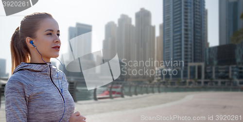 Image of happy woman with earphones running over dubai city