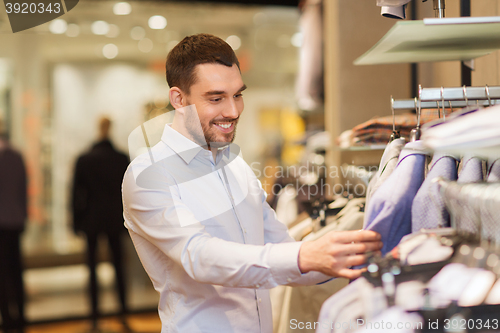 Image of happy young man choosing clothes in clothing store