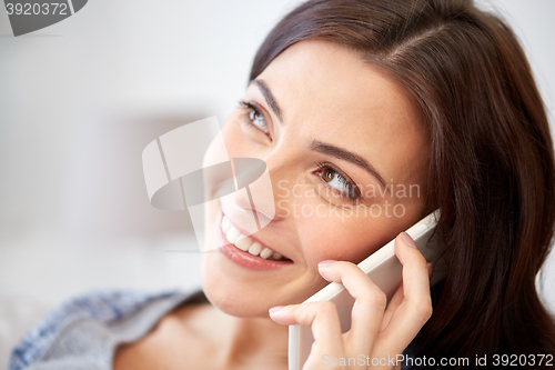 Image of happy young woman calling on smartphone at home