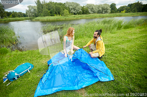 Image of happy couple setting up tent outdoors