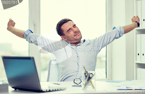 Image of bored businessman with laptop and papers at office