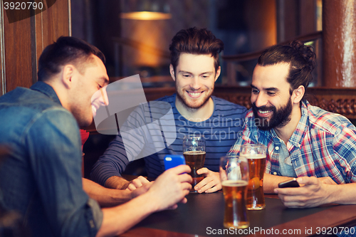 Image of male friends with smartphones drinking beer at bar