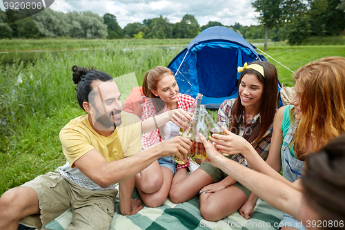 Image of happy friends with tent and drinks at campsite