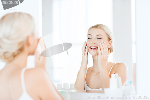 Image of happy woman applying cream to face at bathroom