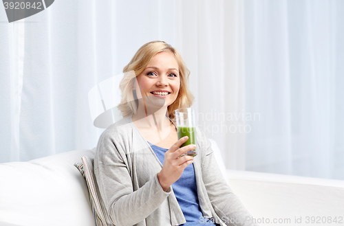 Image of happy woman drinking green juice or shake at home
