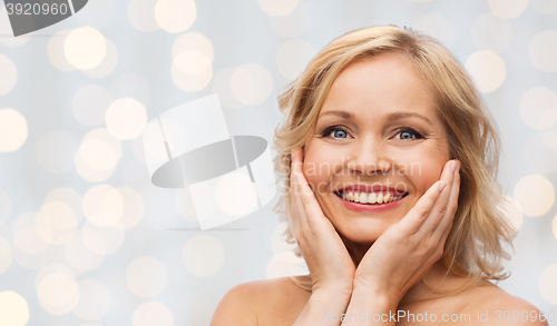 Image of smiling woman with bare shoulders touching face