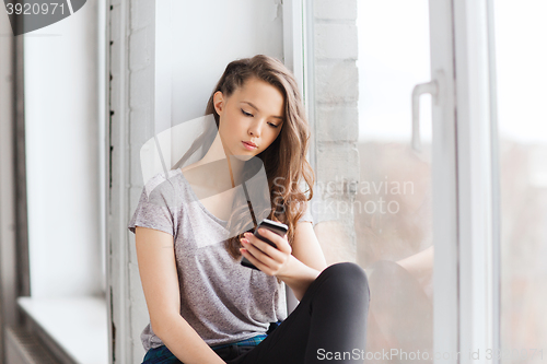 Image of sad pretty teenage girl with smartphone texting