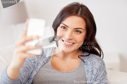 Image of happy woman taking selfie with smartphone at home