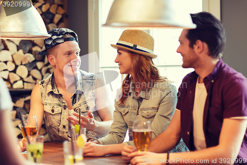 Image of happy friends drinking beer and cocktails at bar