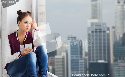 Image of teenage girl sitting on windowsill with smartphone