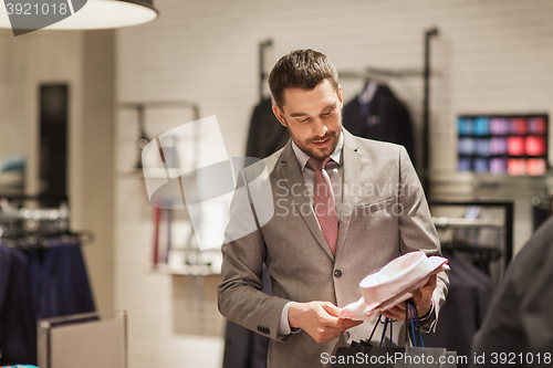 Image of happy young man choosing shirt in clothing store