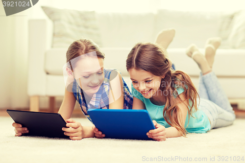 Image of happy girls with tablet pc lying on floor at home