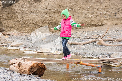 Image of Girl seven years is on rickety bridge over the creek arms outstretched for balance