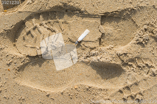 Image of stub of a cigarette lying on the sand on a sea beach