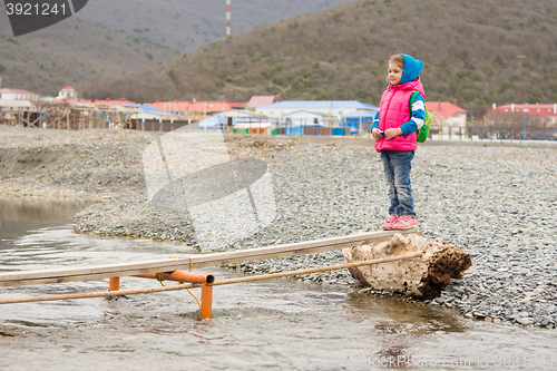 Image of Little girl is undecided at the beginning of flimsy crossing a stream and looking at the other side