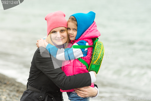 Image of Mom and daughter in warm clothing standing arm in arm on the beach