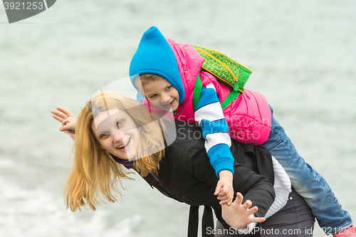 Image of Close-up of a young girl playing with her baby on the nature near the water in cold weather