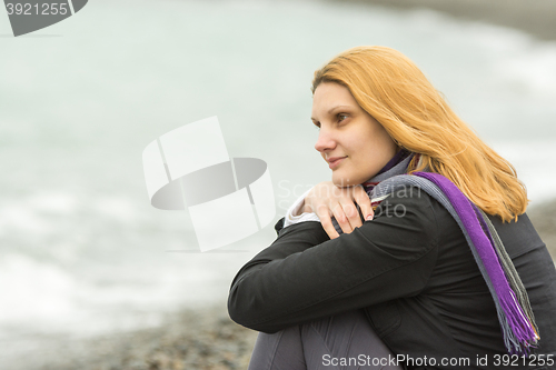 Image of Portrait of sitting girl on the beach on a cloudy cold day put his head in his hands