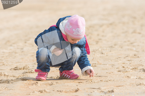 Image of Five-year girl in the spring of the pen draws on the sand by the sea